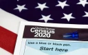 یک خودکار و یک فرم سرشماری 2020 ایالات متحده، با پرچم آمریکا به عنوان پس‌زمینه.