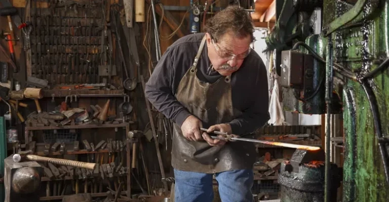 آهنگر در کارگاه خود از یک چکش برقی برای شکل دادن به فولاد داغ استفاده می‌کند