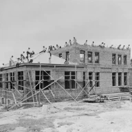 عکس سیاه و سفید قدیمی از جوانان زیادی که در حال ساختن یک ساختمان بزرگ هستند