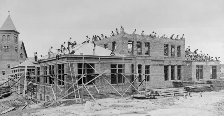 عکس سیاه و سفید قدیمی از جوانان زیادی که در حال ساختن یک ساختمان بزرگ هستند