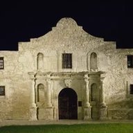 نمای مستطیلی یک ساختمان سنگی، متقارن با درگاه مرکزی قوسی شکل و یک جان‌پناه مرکزی در بالای سقف