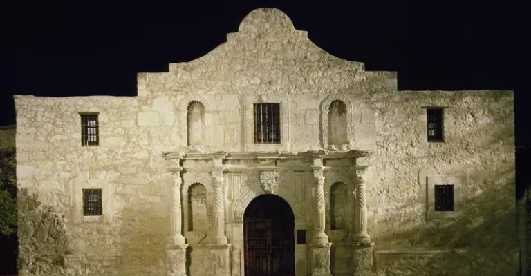 نمای مستطیلی یک ساختمان سنگی، متقارن با درگاه مرکزی قوسی شکل و یک جان‌پناه مرکزی در بالای سقف