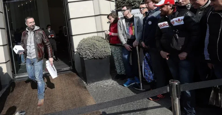 صف مضطرب مصرف‌کنندگانی که منتظر خرید اولین ساعت اپل هستند و مردی خندان که یکی از آنها را خریده است، نمادی از جنبه‌های فرهنگ مصرف‌گرایی هستند.