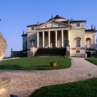 ویلایی با طراحی پالادیو، شامل سنگفرش، ستون‌ها و گنبد در محیطی روستایی با مجسمه پرنده در پیش‌زمینه