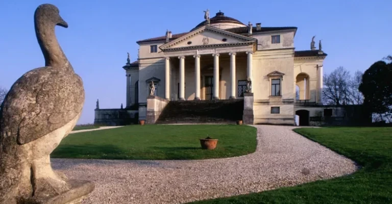 ویلایی با طراحی پالادیو، شامل سنگفرش، ستون‌ها و گنبد در محیطی روستایی با مجسمه پرنده در پیش‌زمینه